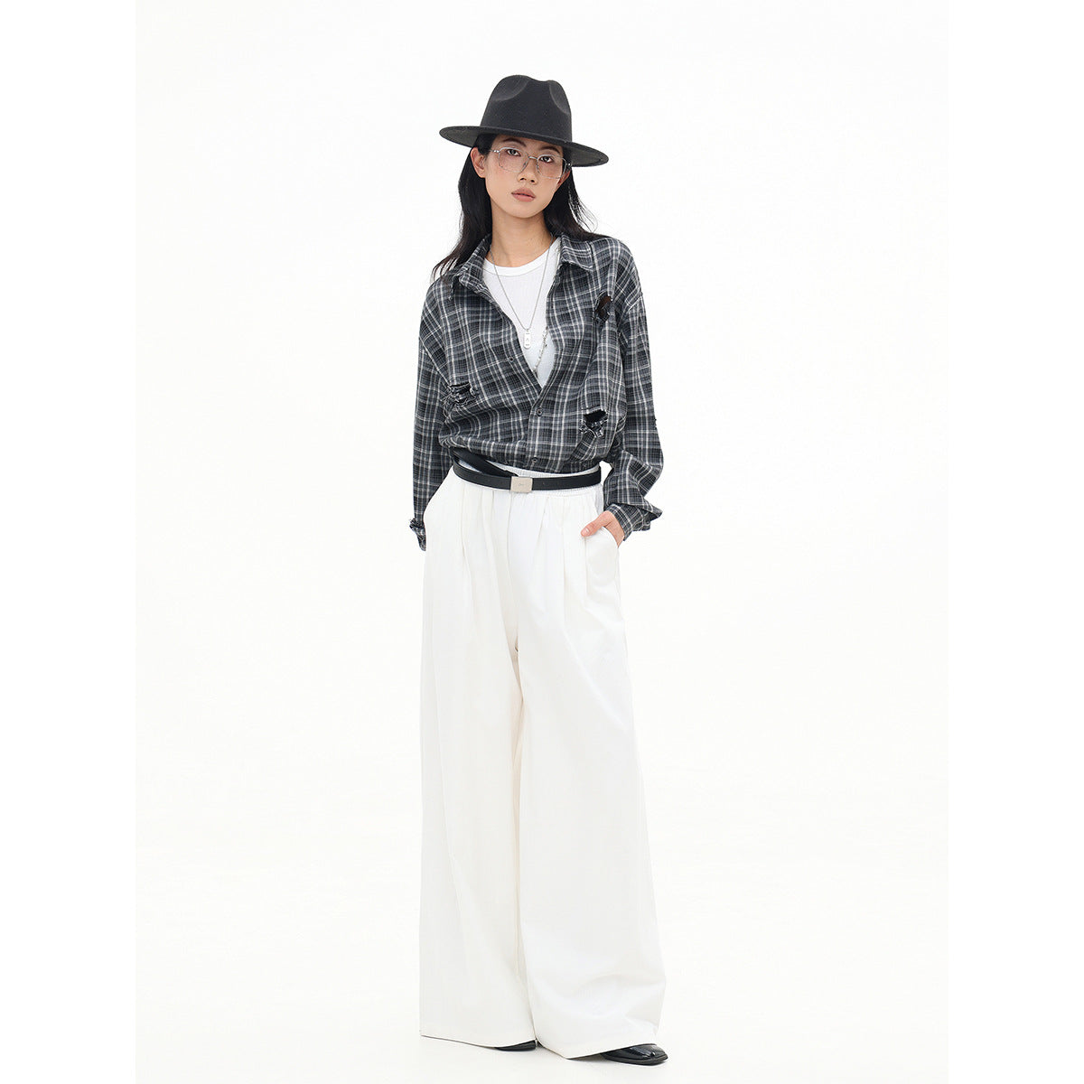 Model wearing a charcoal gray plaid button-up shirt with distressed details, white wide-leg trousers, and a black hat.