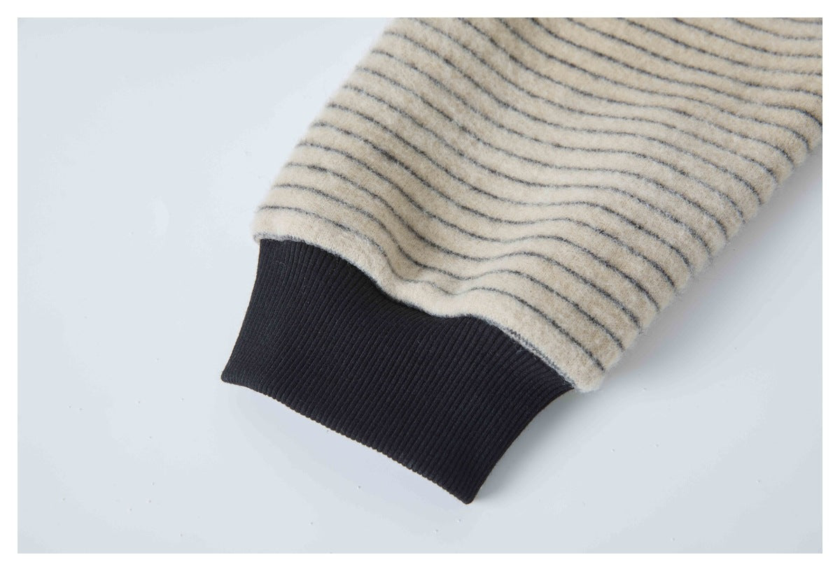 Close-up of a black ribbed cuff beneath cream fabric with thin dark stripes.