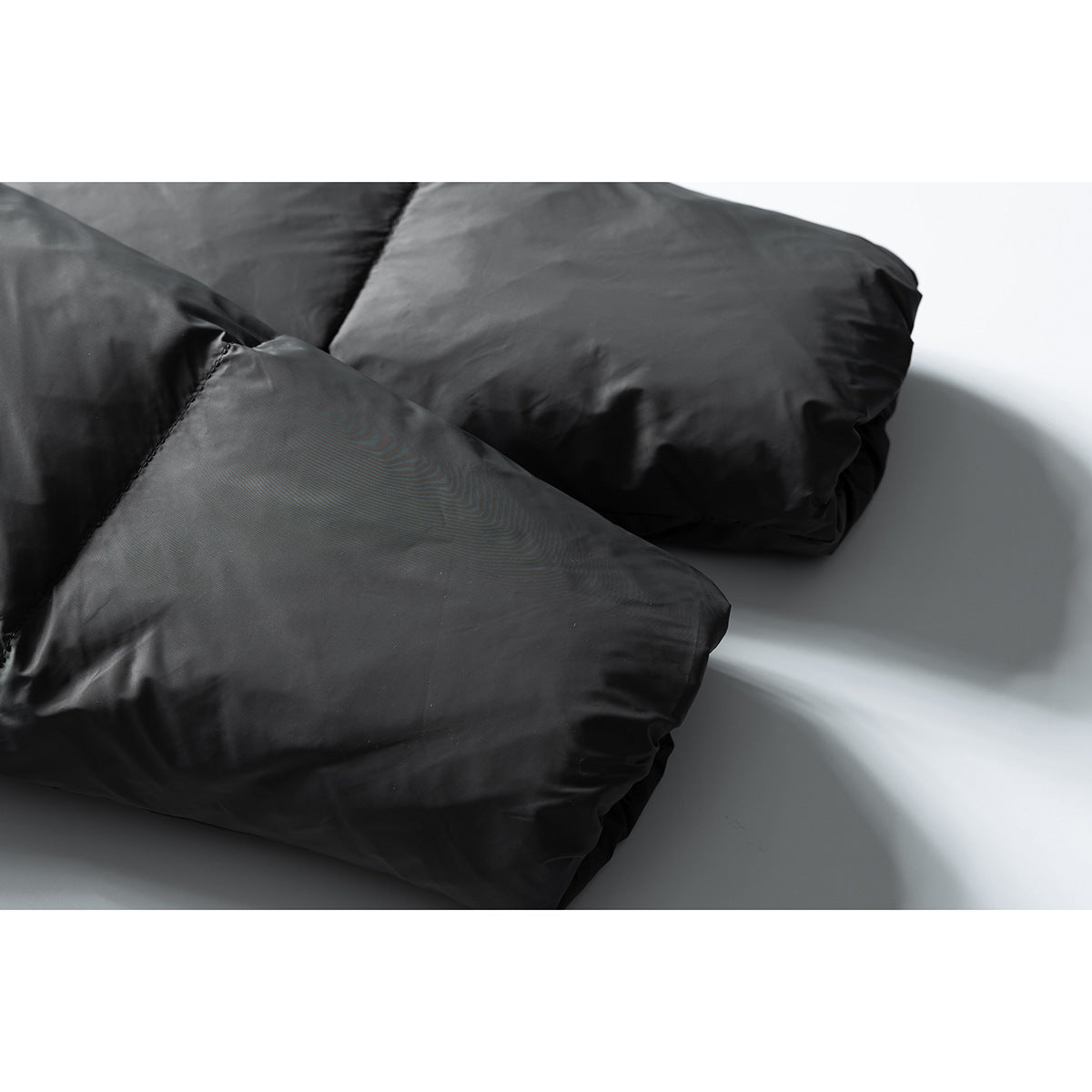 Close-up of the charcoal puffer jacket's padded sleeve and overlapping fabric panels.