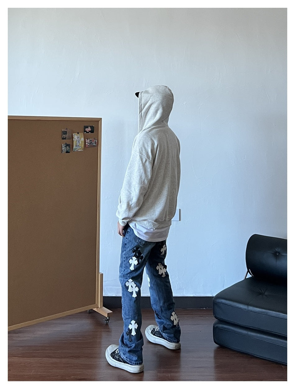 Side-back view of a person wearing a heather white-gray hoodie with the hood up, over a white tee and cross-print jeans