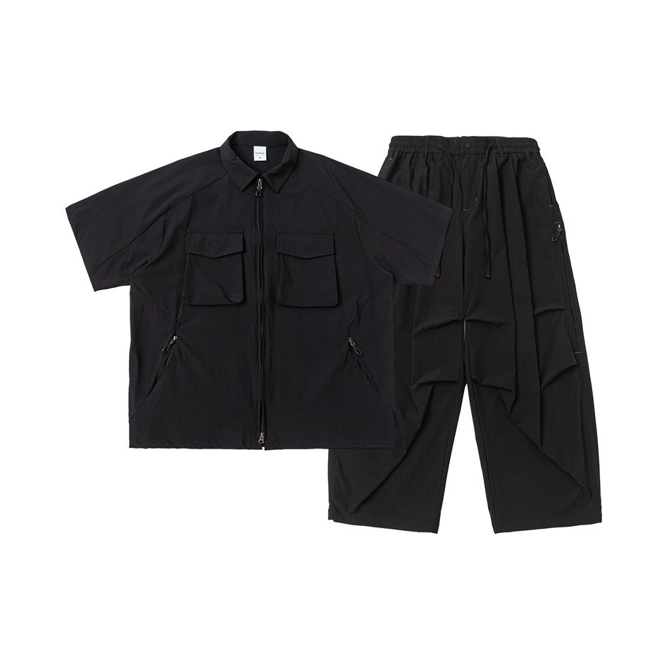 Black two-piece set laid flat: short-sleeve zip shirt with flap pockets and relaxed drawstring trousers.