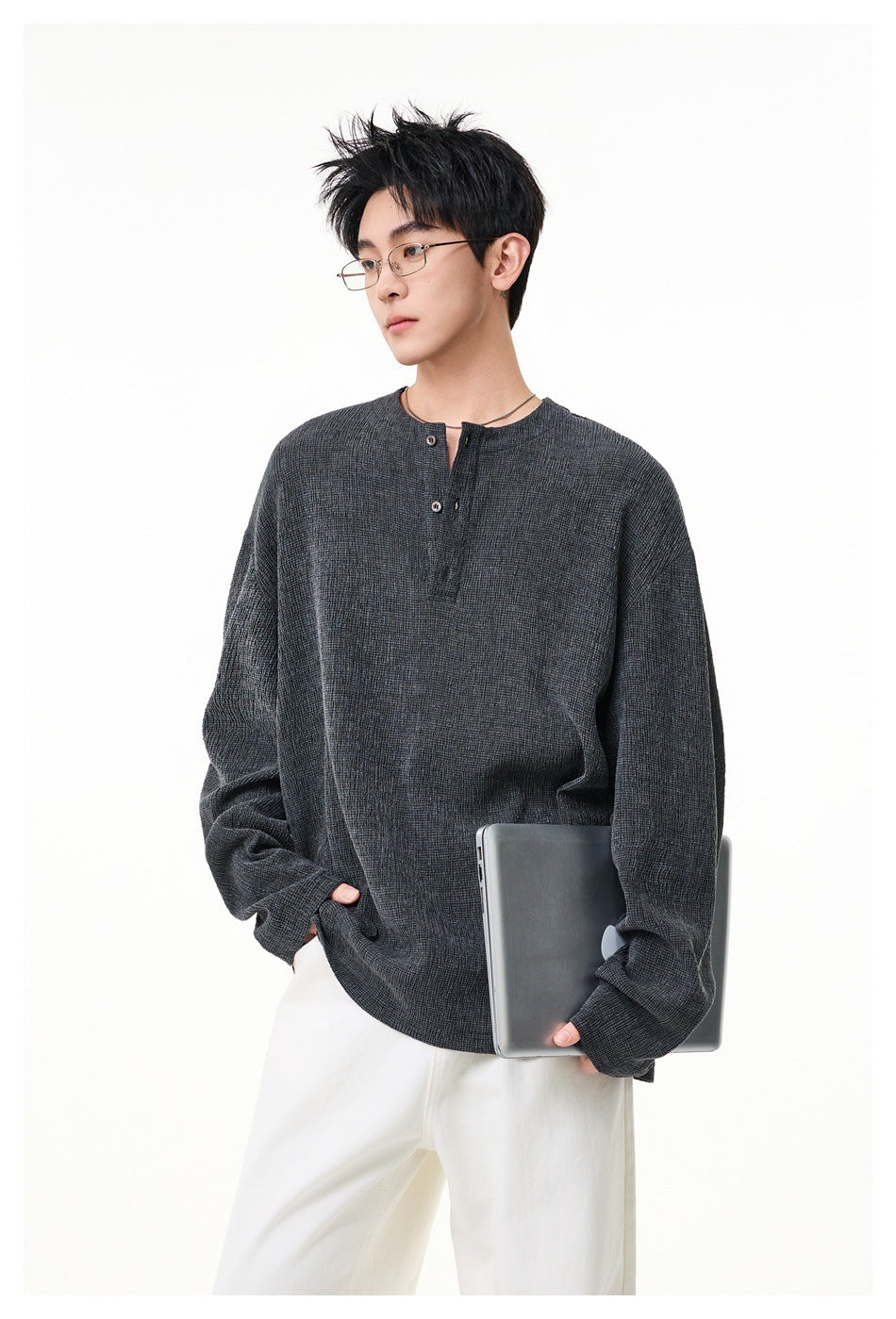 Model wearing a dark charcoal long-sleeve henley with a short button placket and white trousers.