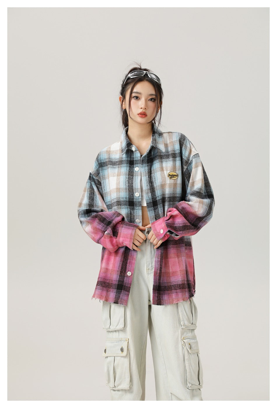 Model wearing an oversized blue-gray plaid shirt with pink sleeves and lower panels, paired with light cargo pants.