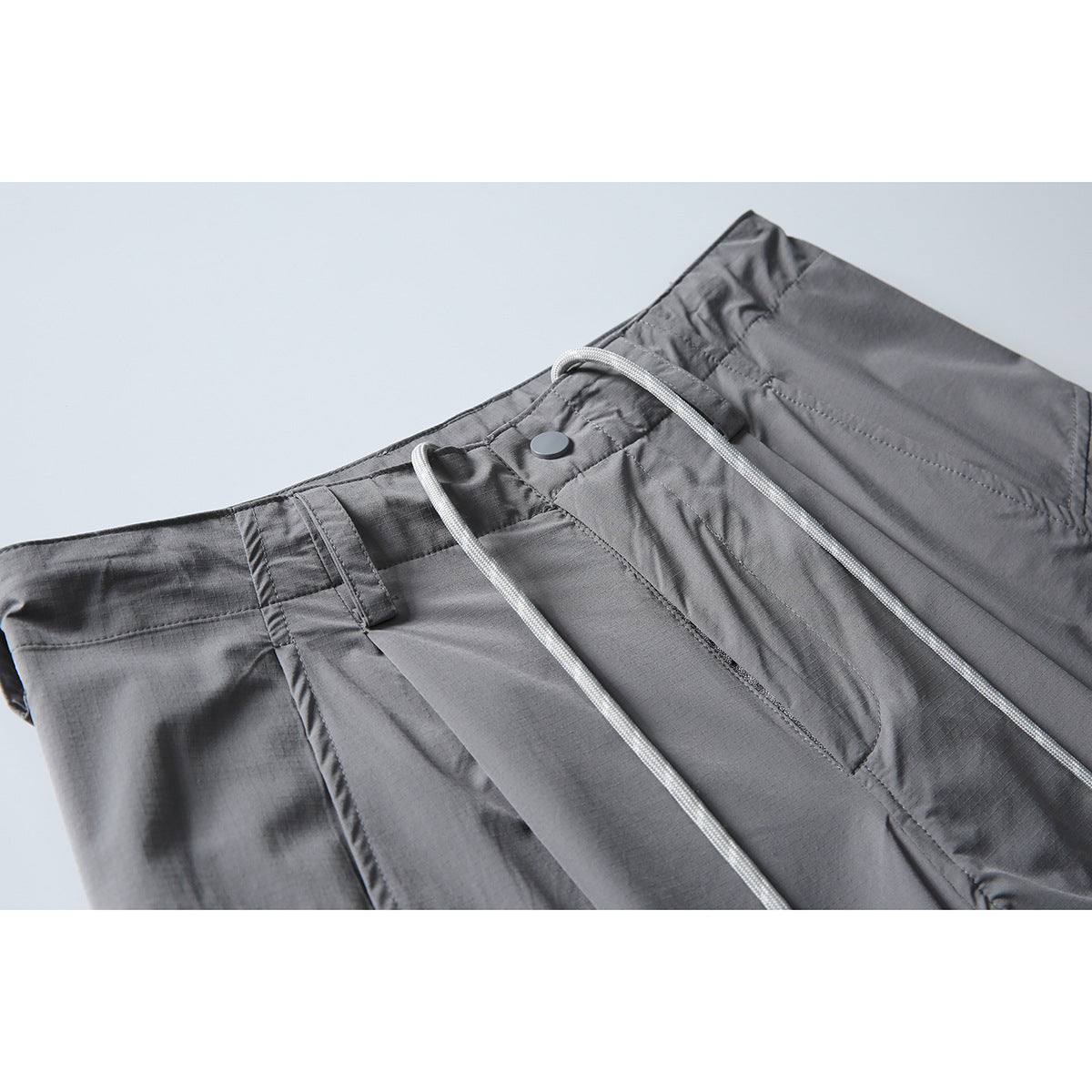 Close-up of gray cargo pants showing the waistband, belt loop, snap, and long drawstrings.