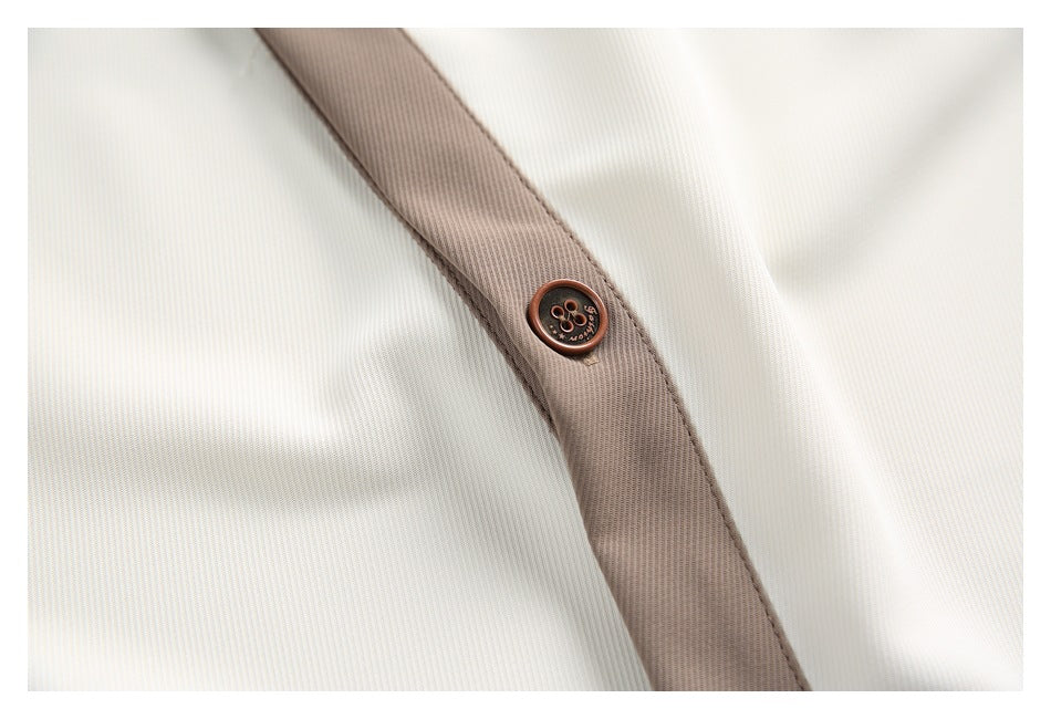 Close-up of a brown button on the taupe placket of a cream shirt.