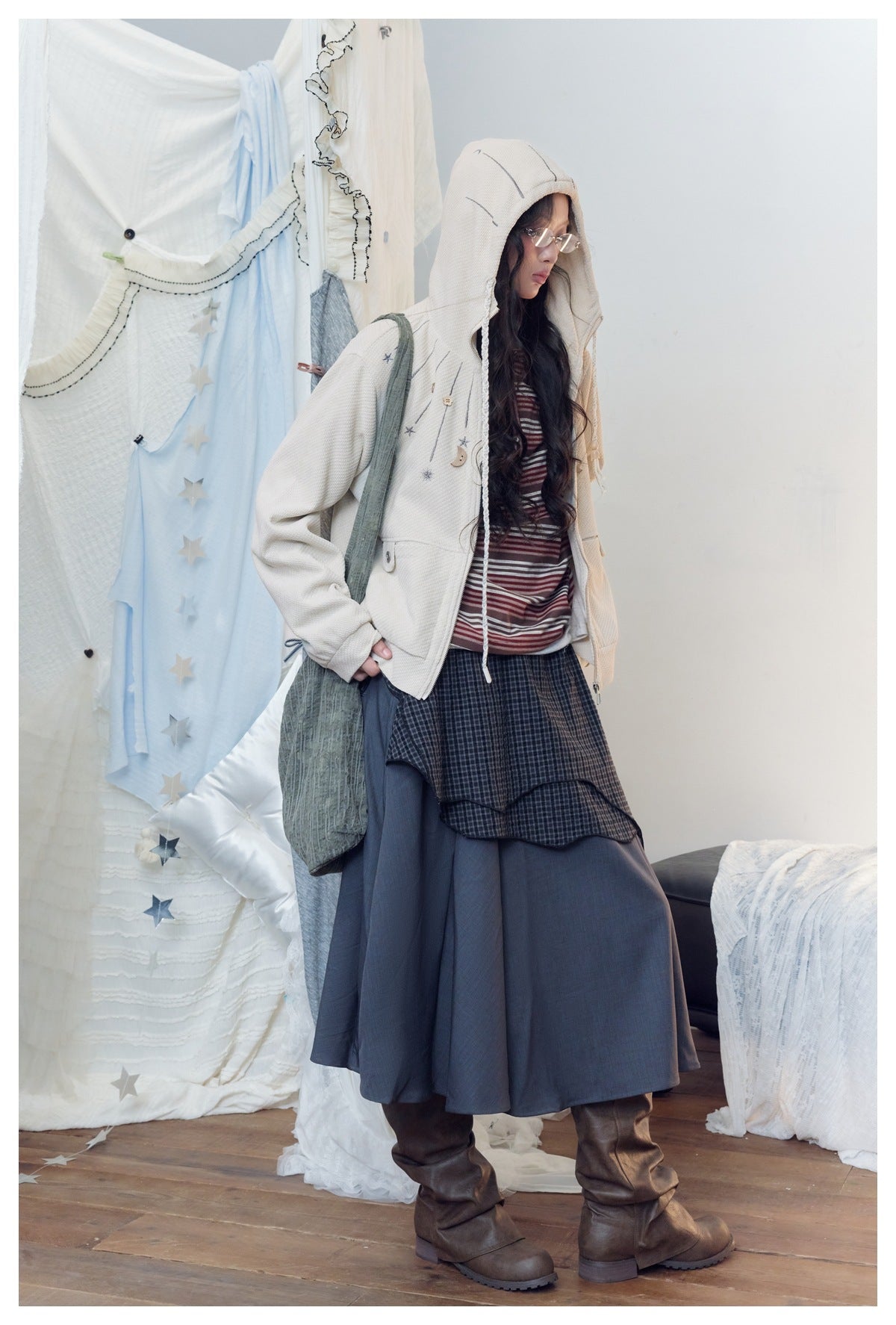 Model wearing an ivory hooded zip jacket with gray celestial motifs, layered over a striped top and dark skirt.