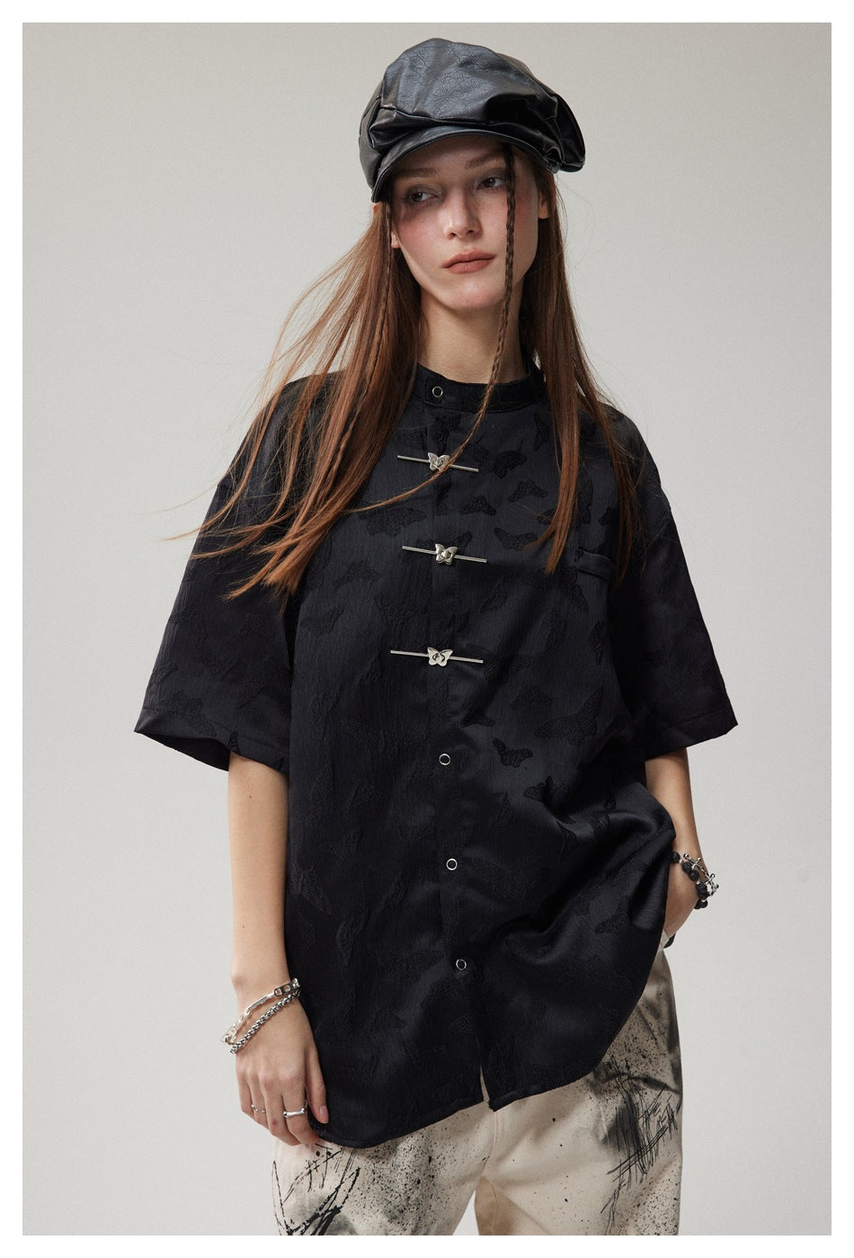 Model wearing a black short-sleeve shirt with raised butterfly motifs and silver frog closures.