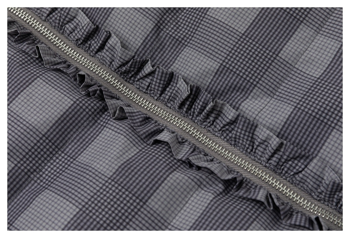 Close-up of a gray and black checked garment with a diagonal zipper bordered by gathered ruffle trim.