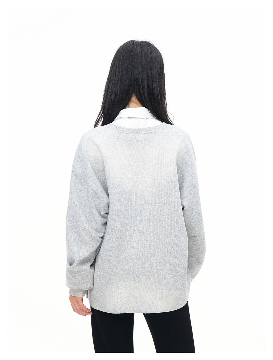 Back view of a model wearing a loose light gray pullover with dropped shoulders and ribbed cuffs.