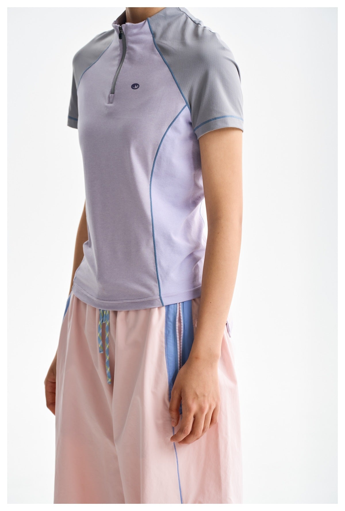 Close view of a lavender zip-neck top with gray sleeves and blue piping, worn with pink trousers.