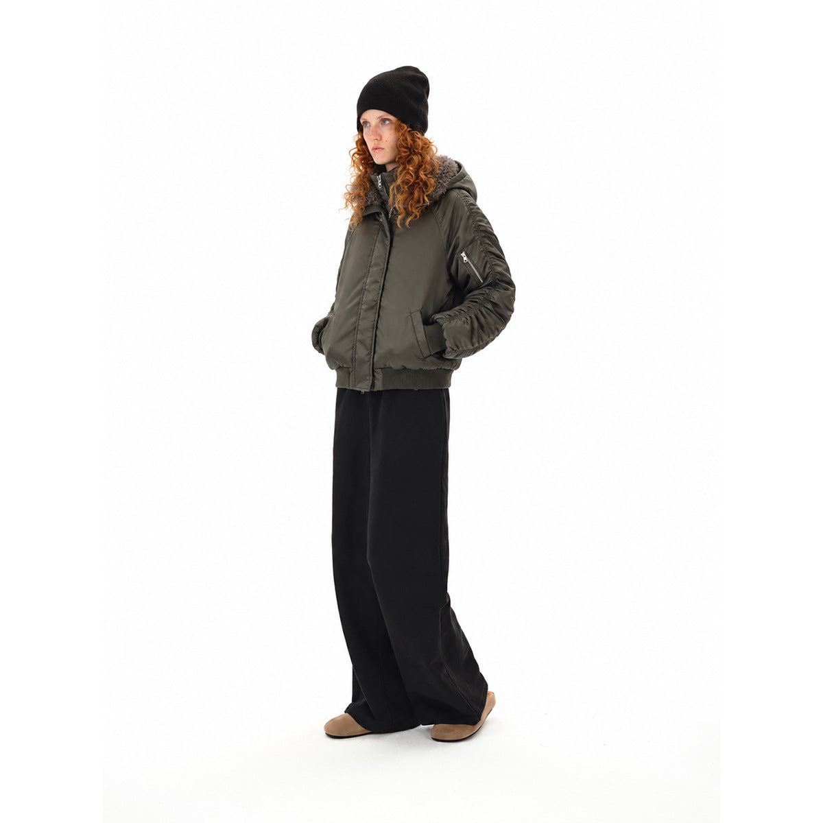 Three-quarter view of a model wearing a dark olive bomber jacket with a plush gray collar and black wide-leg trousers.