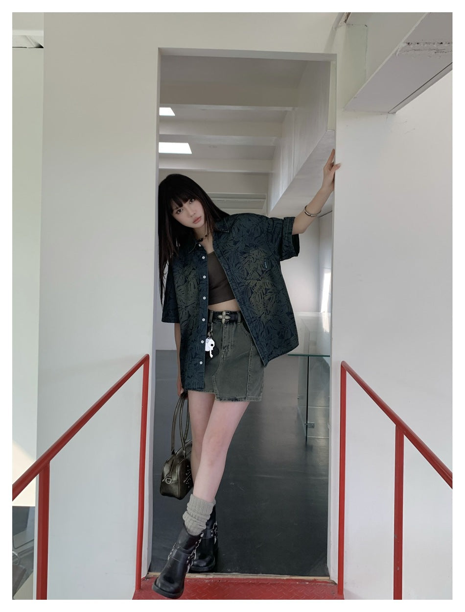 Model wearing the leaf-print short-sleeve shirt open over a crop top and skirt, leaning in a white doorway with red railings