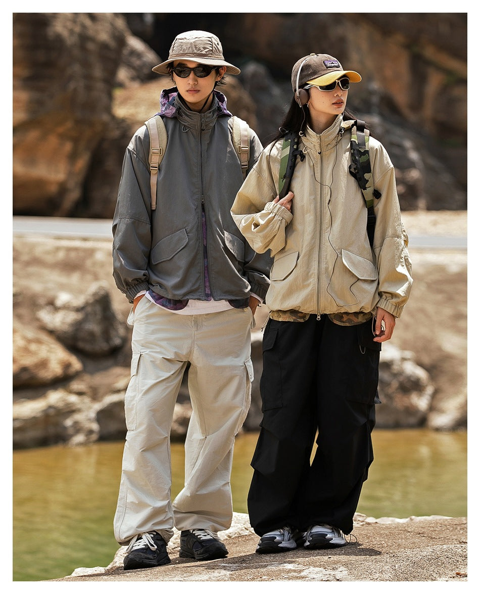 Two models outdoors wearing loose zip jackets: one charcoal and one beige, with cargo pants.