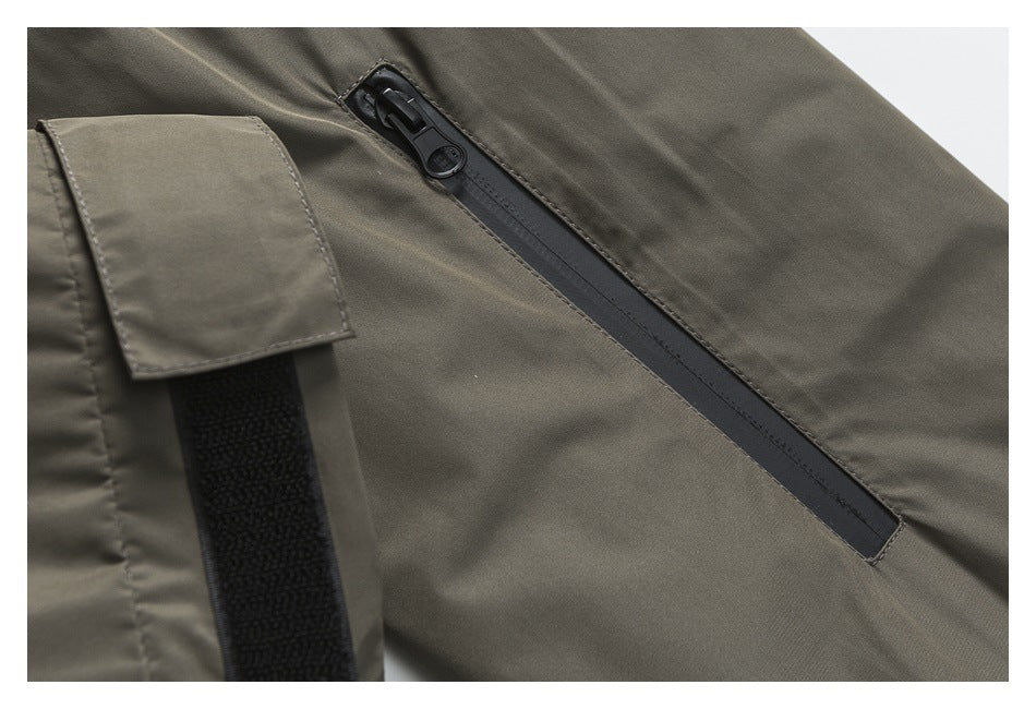 Close-up of a black diagonal zipper and hook-and-loop tab on a gray-olive garment.