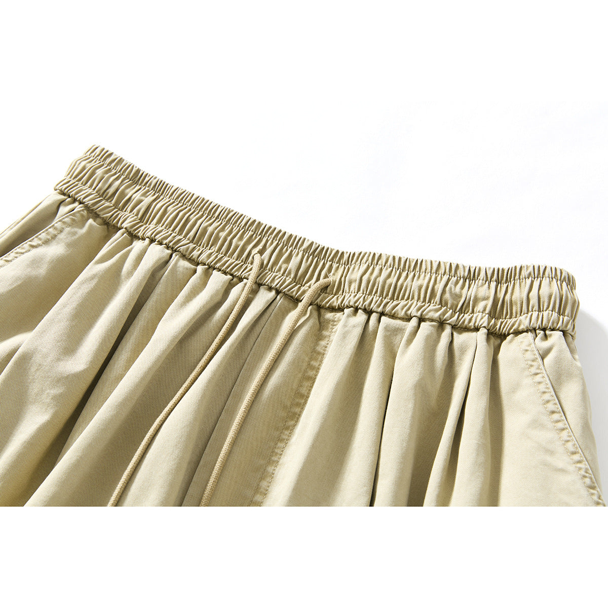 Close-up of beige shorts showing the elastic waistband, drawstring, pleats, and side pocket opening.