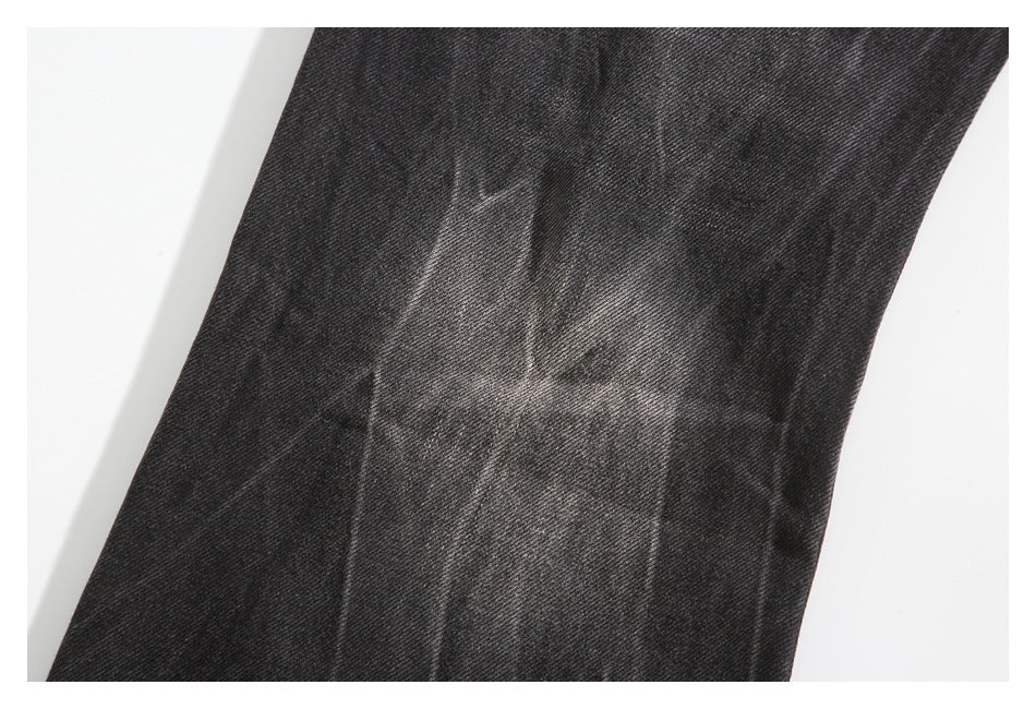 Close-up of a charcoal-black jeans leg showing a faded, worn patch.