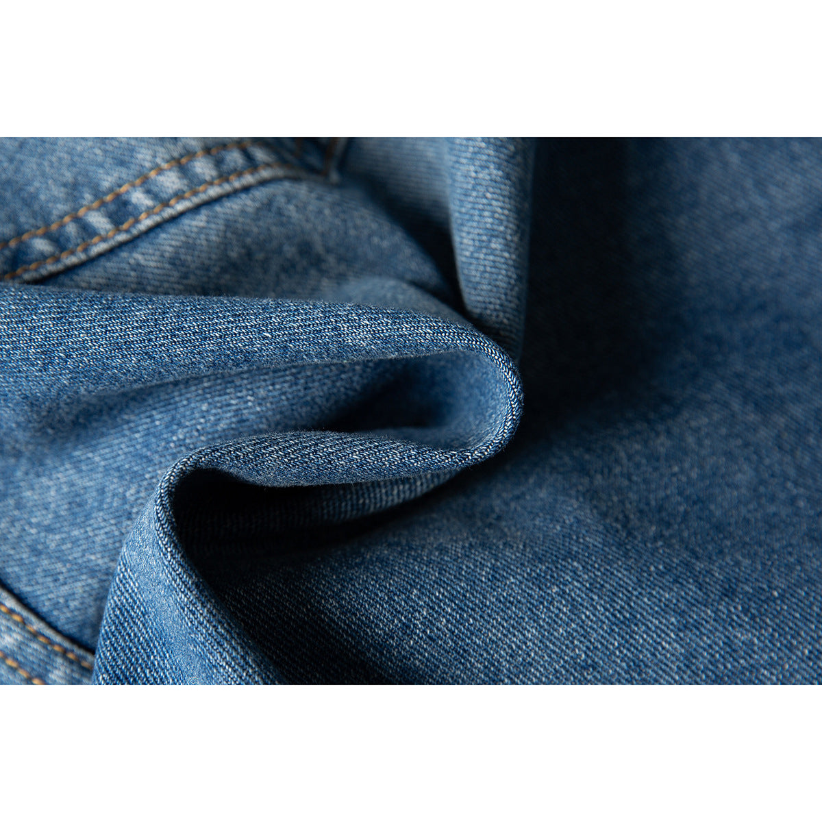 Macro view of blue denim fabric folded to show its woven texture and contrast stitching.