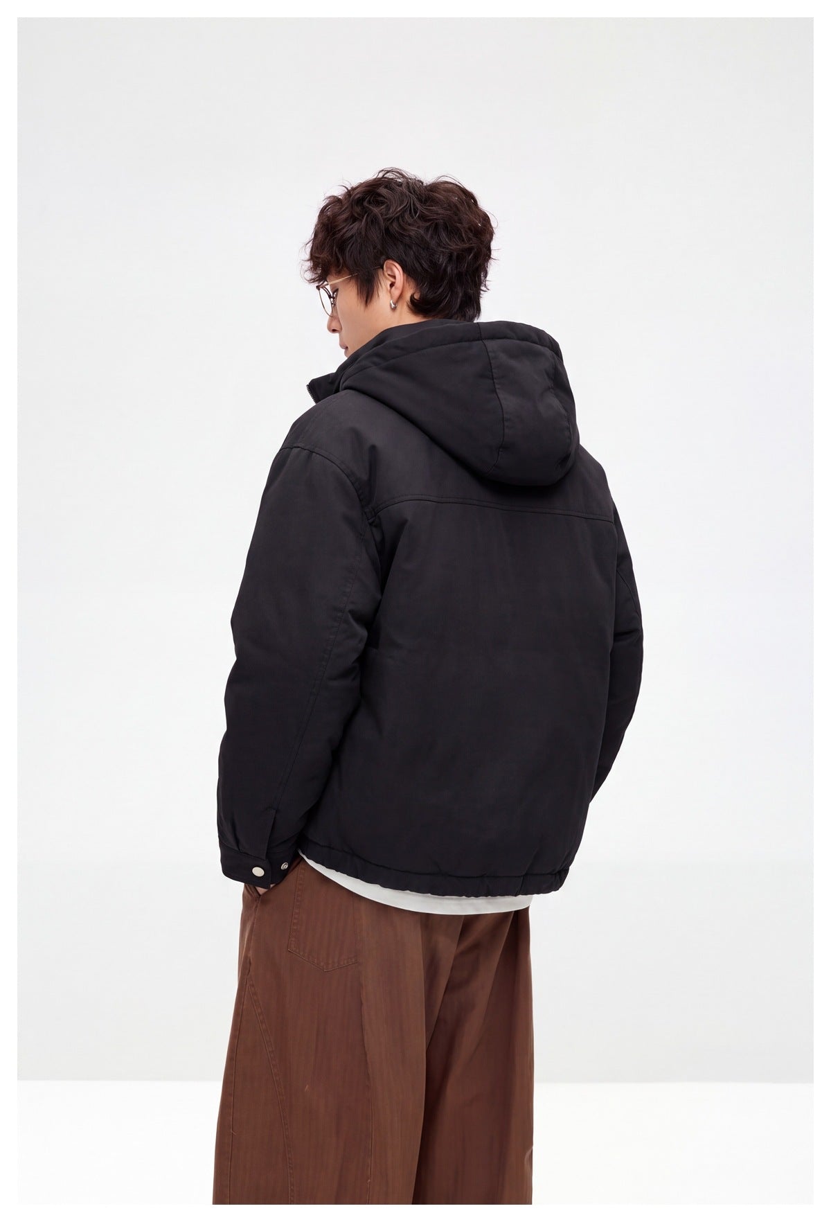 Rear view of a model wearing a black hooded jacket with a plain back and snap-cuff sleeves.