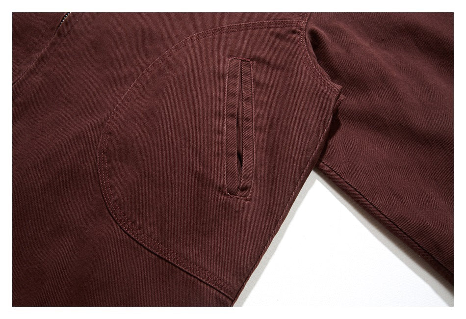 Close-up of a burgundy jacket front with a large curved pocket and a narrow vertical zip pocket.