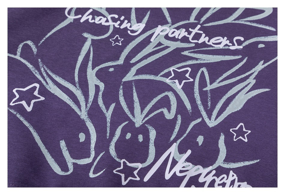 Close-up of a purple sweatshirt graphic showing white English lettering, stars, and several playful rabbit illustrations.
