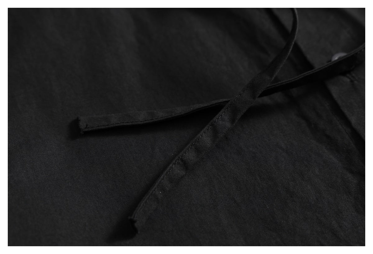 Close-up of a narrow black fabric tie detail lying across the black shirt.