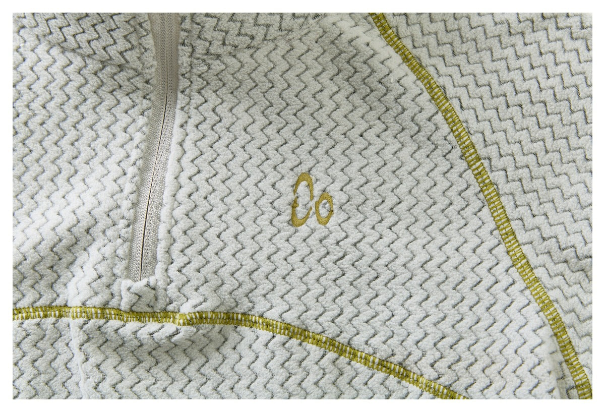 Close-up of a cream and gray zigzag-patterned top with a small gold embroidered chest emblem and mustard stitching.