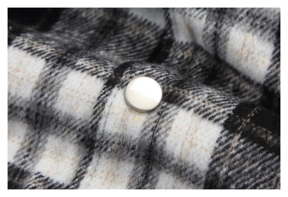 Close-up of a cream snap fastener on black, gray, and cream plaid fabric.