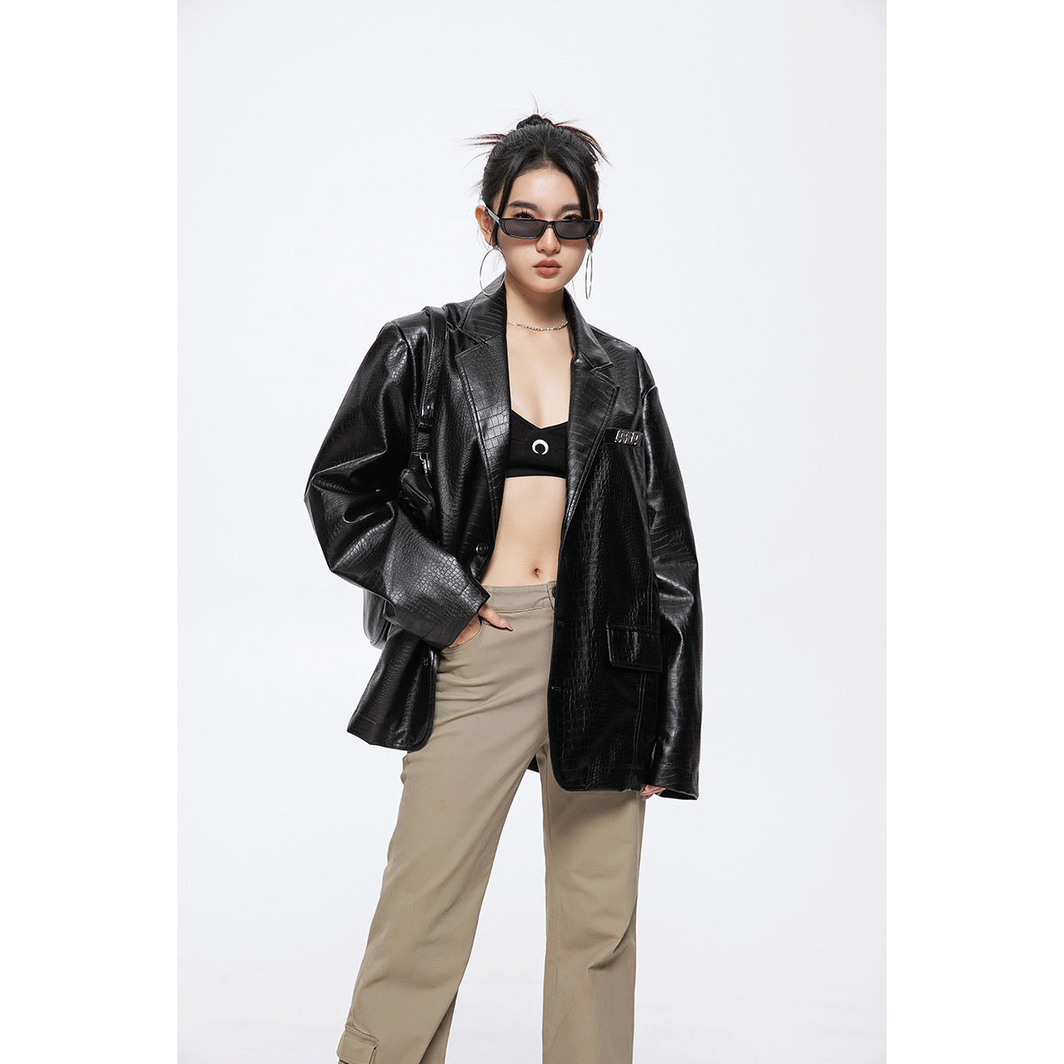 Front view of a model in an oversized black crocodile-embossed blazer, black crop top and beige trousers.