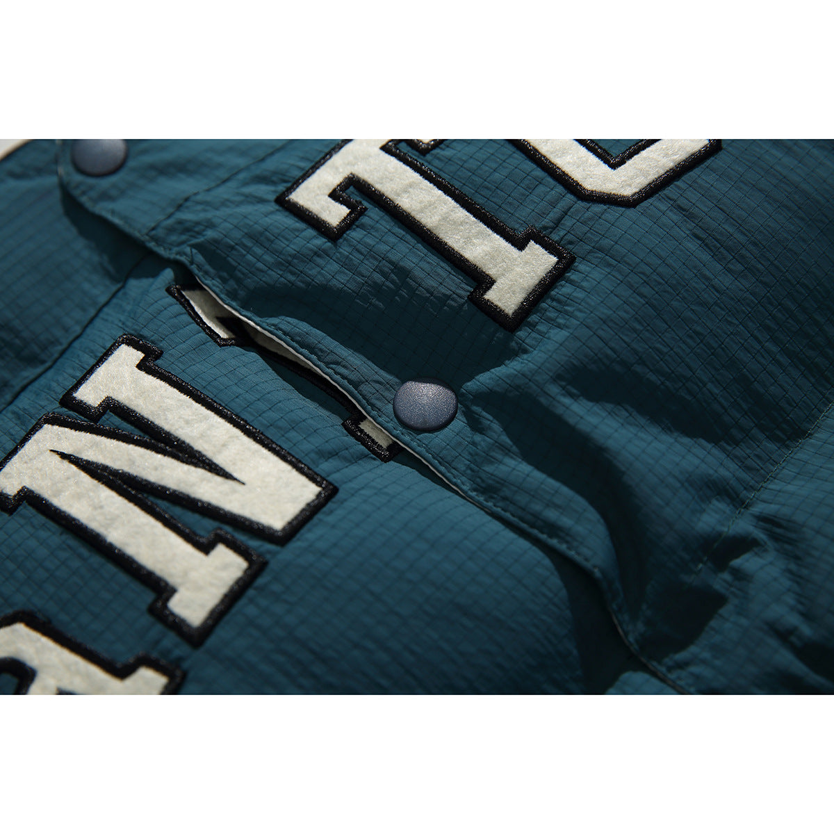 Close-up of cream and black lettering, snap buttons, and the grid-textured teal vest fabric.