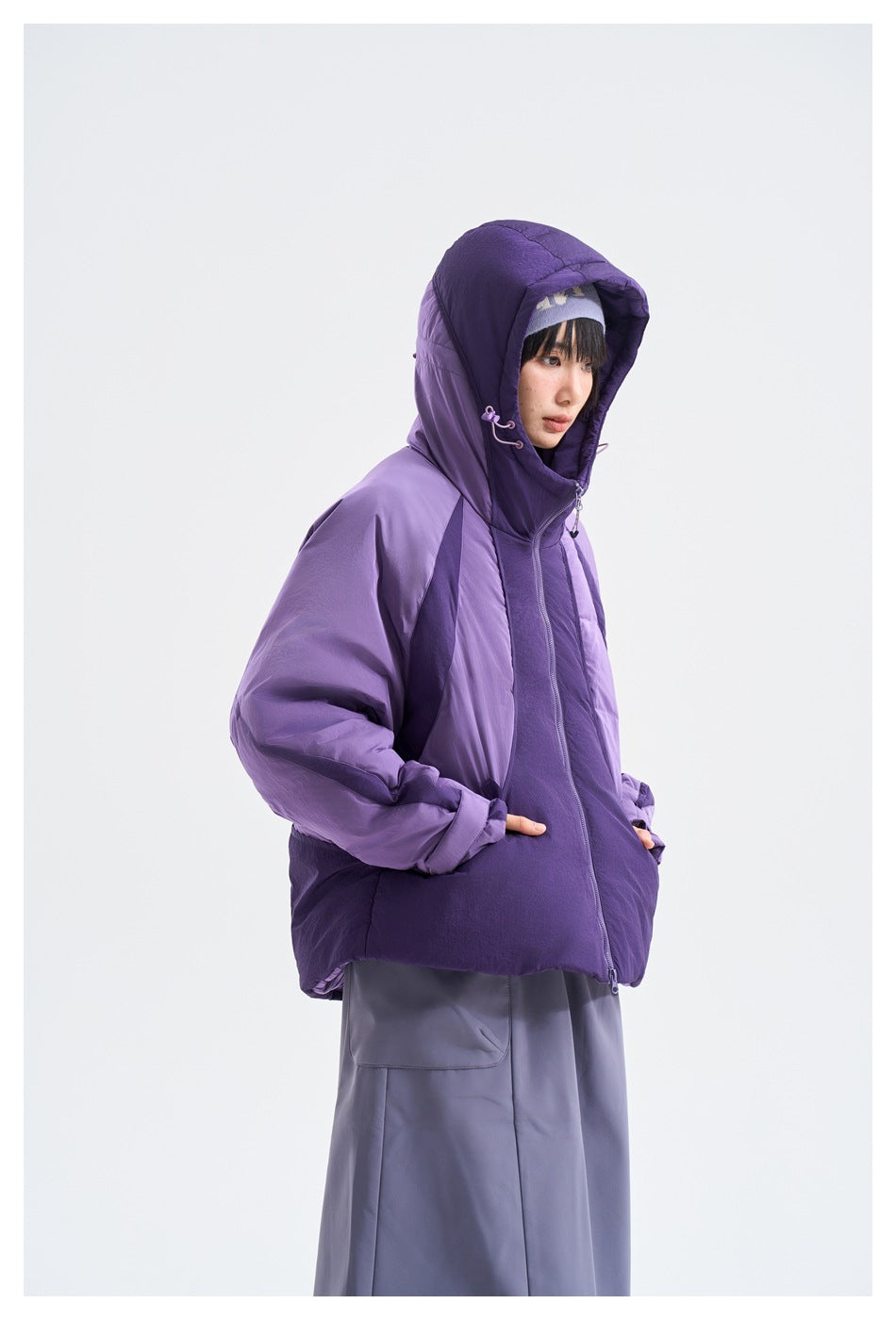Side view of a model wearing a two-tone purple hooded jacket and a gray-purple skirt.