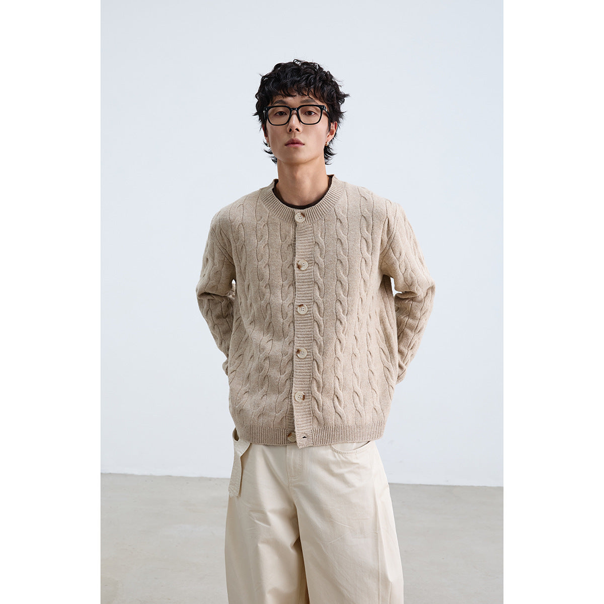 Front view of a model in a beige cable-knit button cardigan and cream trousers.