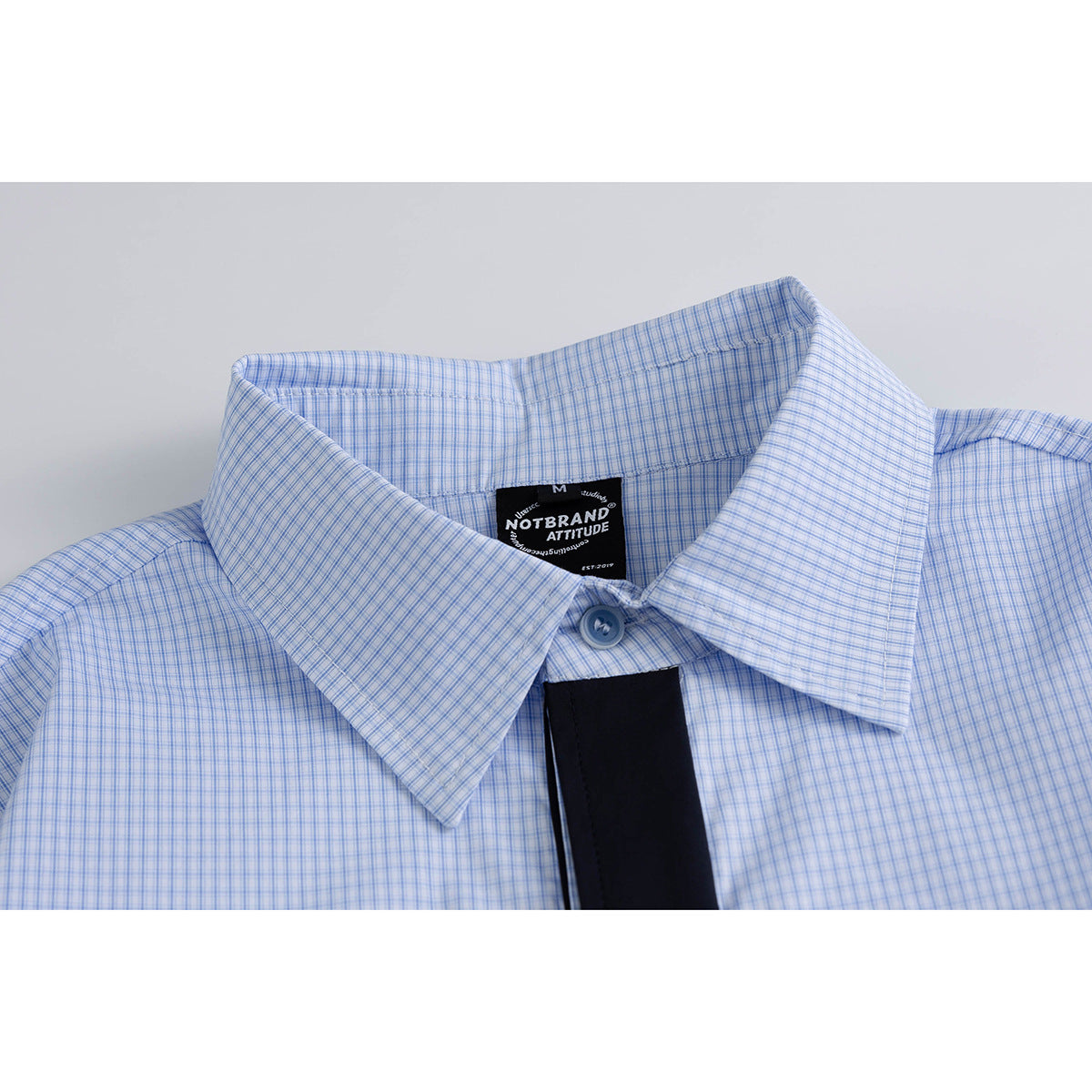 Close-up of a light blue fine-check shirt collar, button and black neck label.