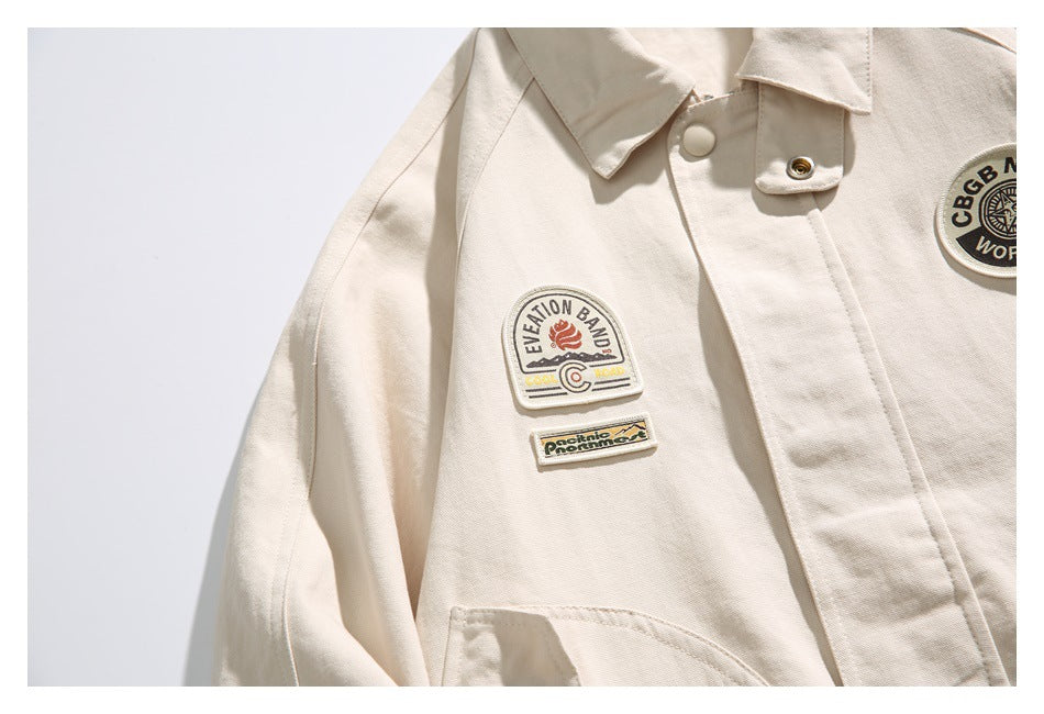 Close-up of an ivory jacket with two embroidered chest patches, a snap-button placket, and part of a round patch.