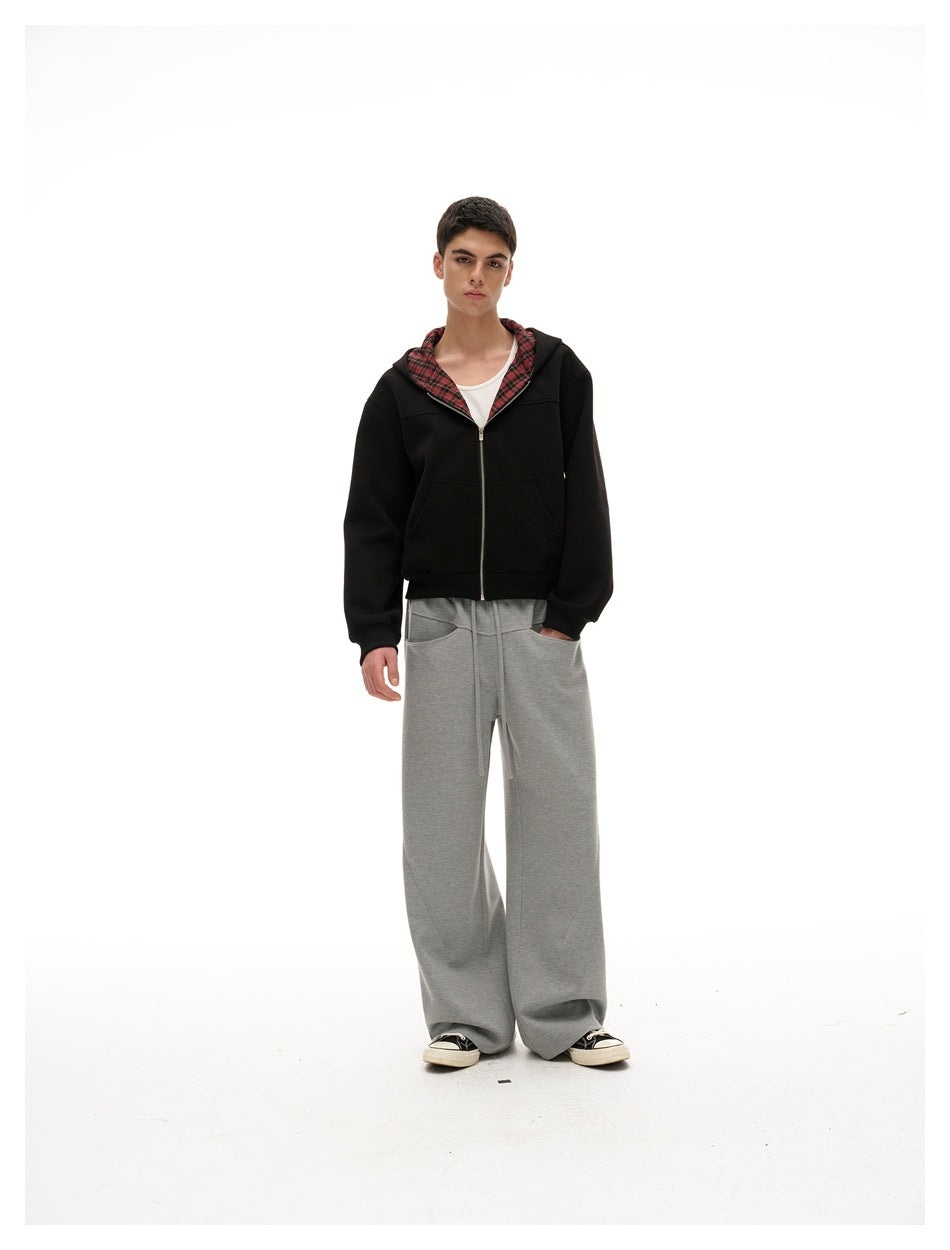 Full-length model wearing a black zip-up hoodie with red plaid lining and loose gray drawstring pants.