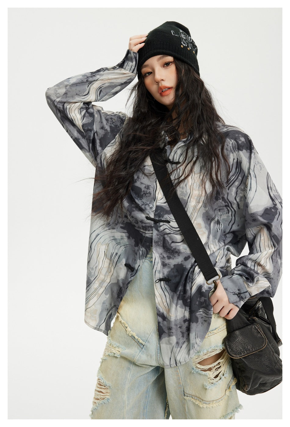 Model wearing a loose gray abstract-print shirt with black frog closures, paired with pale distressed jeans.