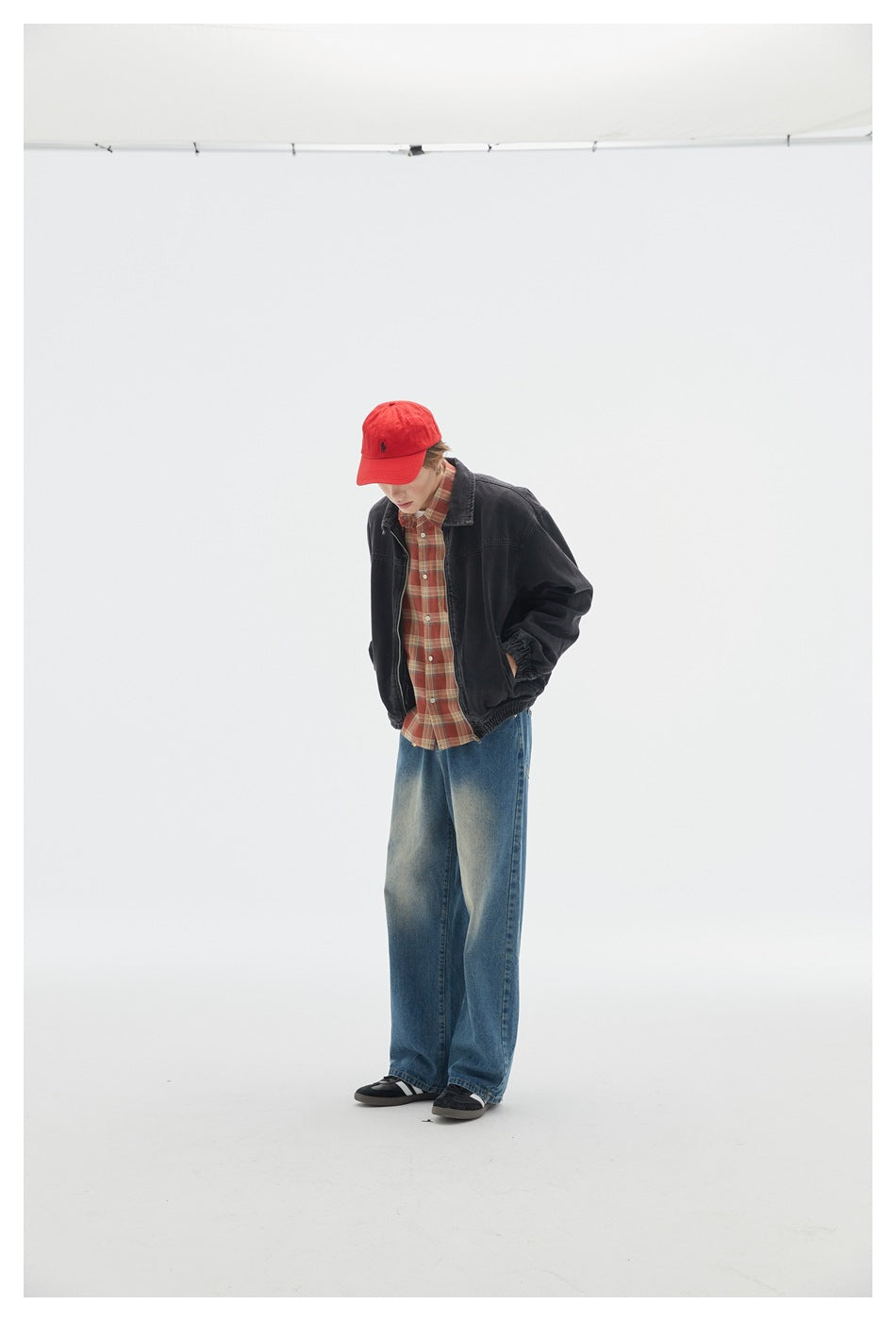 Full-length view of a model wearing a black jacket over a red plaid shirt and loose blue jeans.
