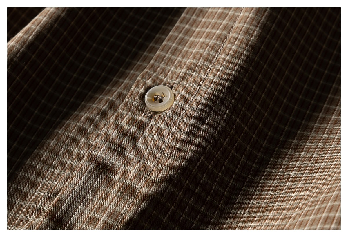 Close-up of a light button and stitched placket on the brown checked shirt.