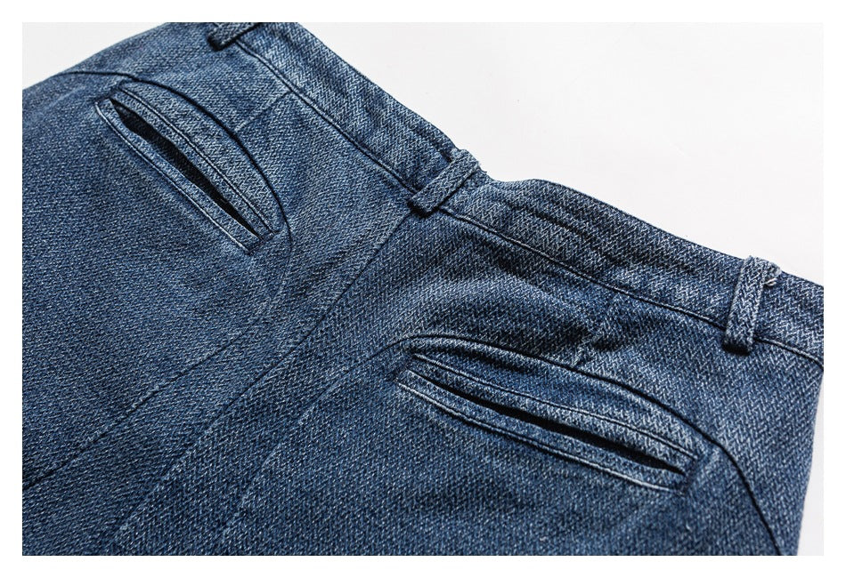 Close-up of the back of dark blue denim trousers with two narrow welt pockets and belt loops.