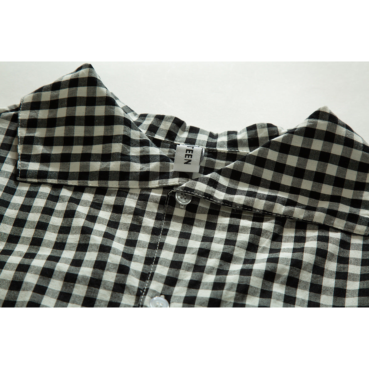 Close-up of a black-and-cream checked shirt collar, neck label, and white buttons.