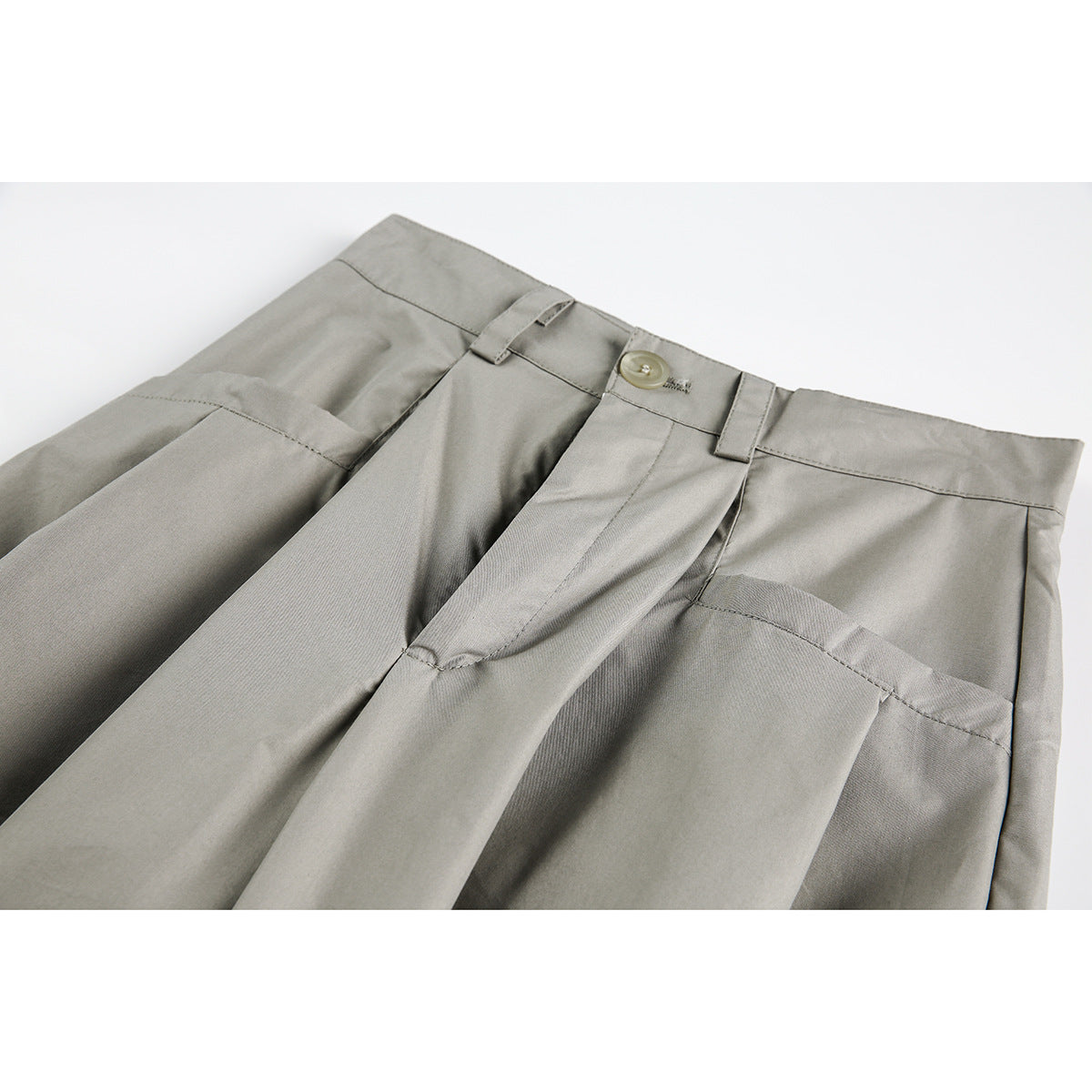 Close-up of gray trousers showing the front waistband, button, belt loops, pleats and slanted pockets.