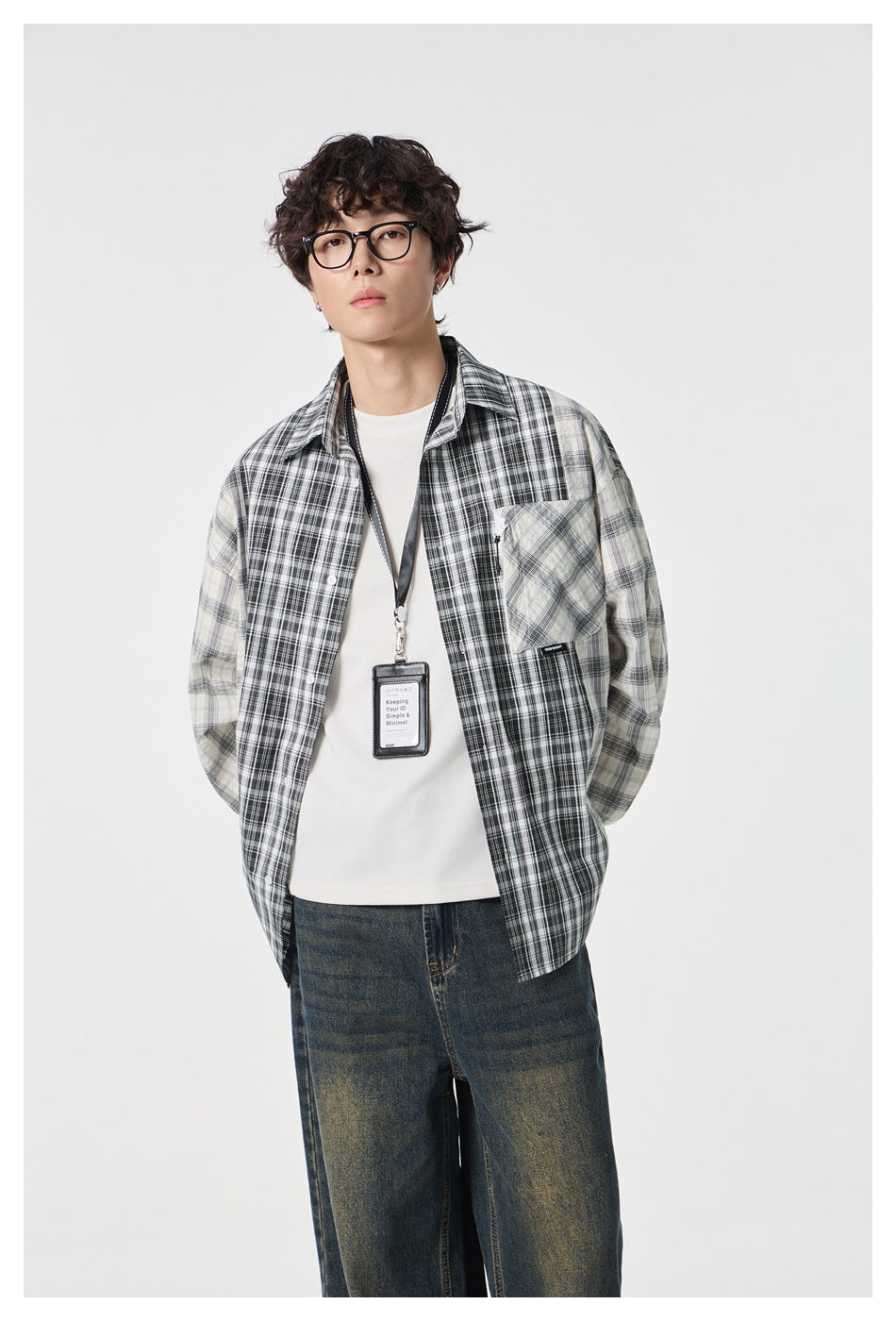 Front view of a model wearing a black, gray, and cream mixed-plaid button-up shirt over a white tee.