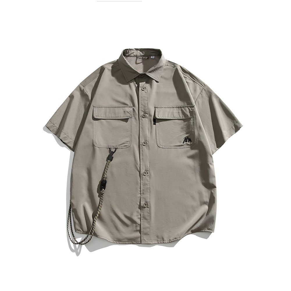 Light khaki-green short-sleeve button-up shirt with two flap chest pockets, logo and a hanging cord, flat lay front