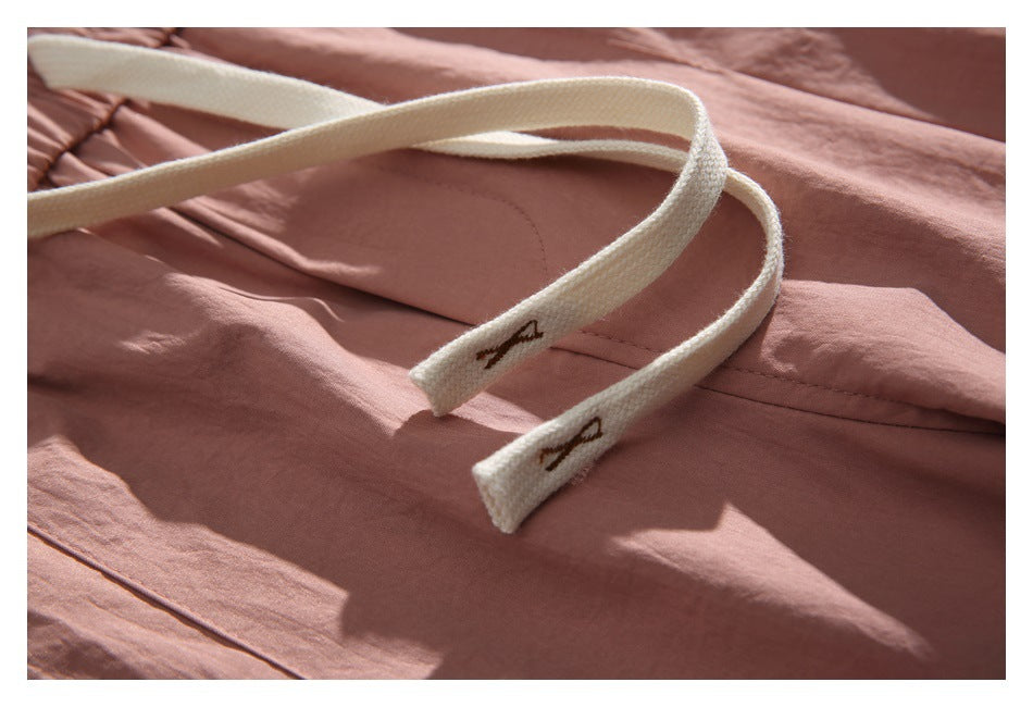 Close-up of cream drawstrings with small embroidered marks against dusty rose fabric.
