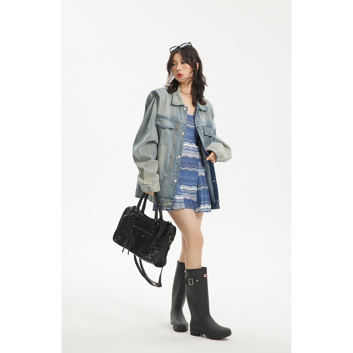 Model wearing an oversized light blue denim jacket over a blue patterned mini dress, with black boots and a handbag.