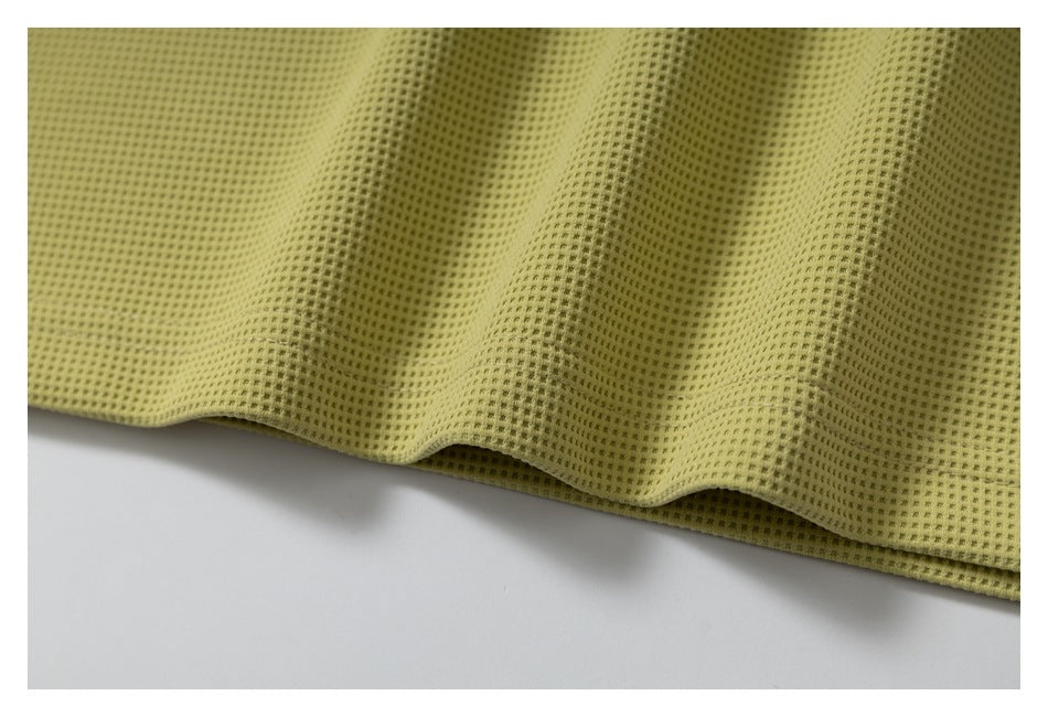 Close-up of the olive-yellow perforated knit fabric draping along a wavy garment edge.