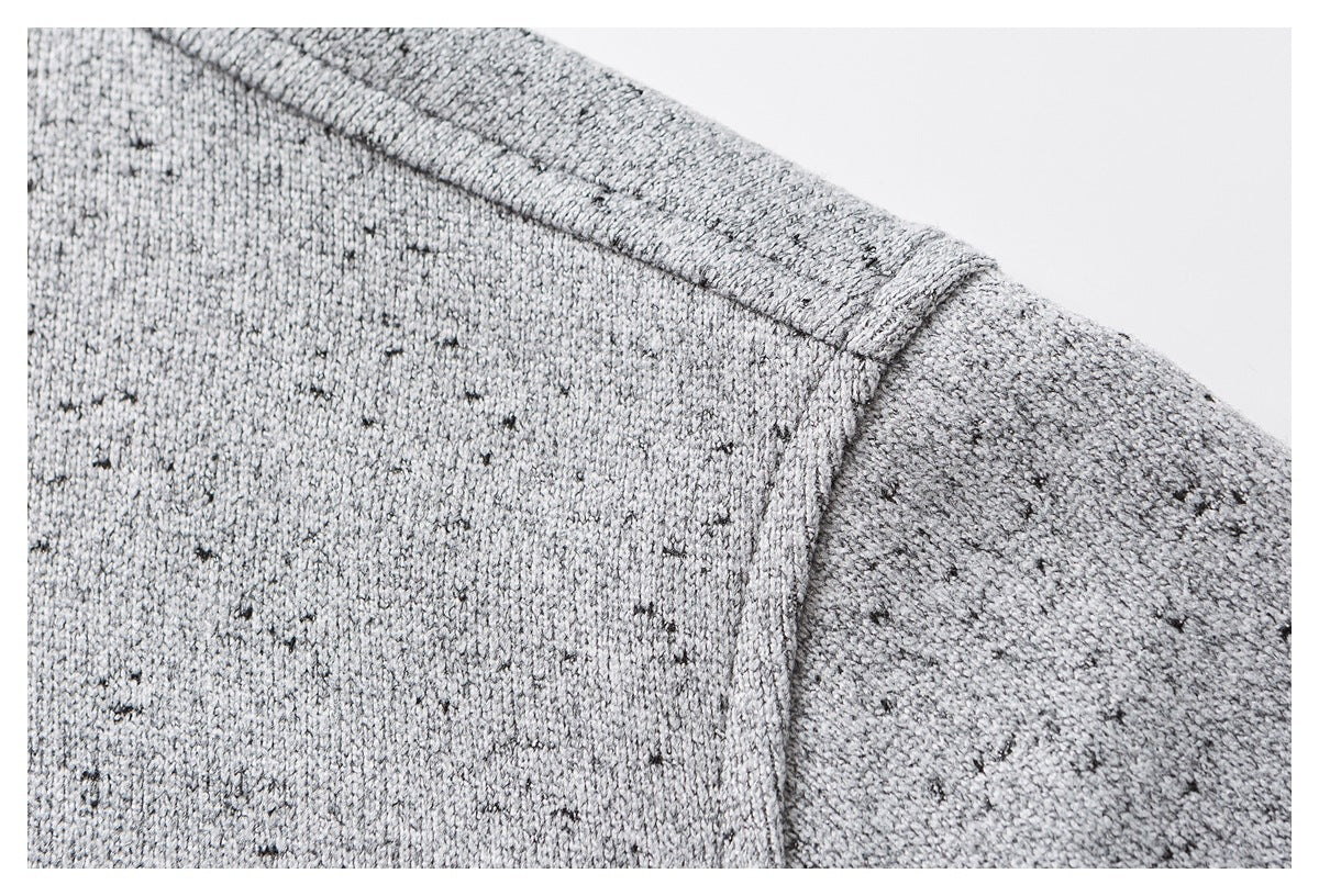 Close-up of a light gray knit garment showing a dark-flecked texture and a stitched shoulder seam.