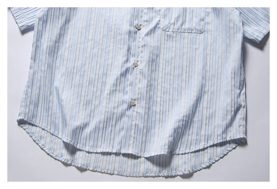 Cropped flat lay of a white short-sleeve button-up shirt with pale blue stripes and a chest pocket.