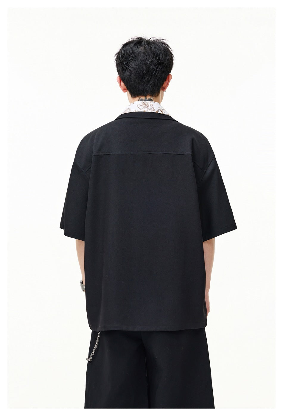 Back view of a model wearing a loose black short-sleeve shirt with a white floral collar showing above the neckline.