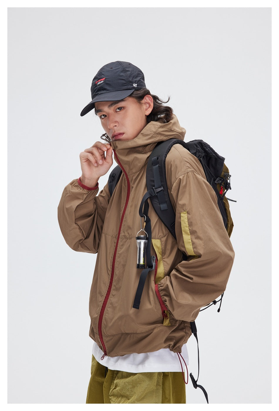 Close view of a model wearing a tan hooded jacket with red zipper trim and yellow sleeve accents.