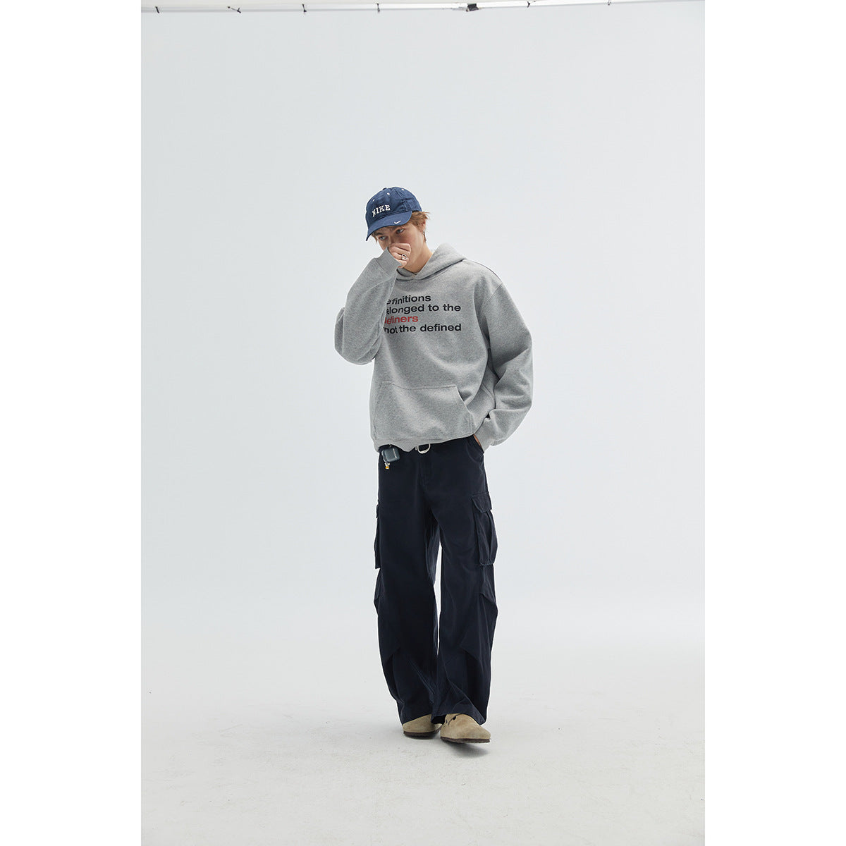 Model wearing a gray text-print hoodie, dark cargo pants, and a blue cap.